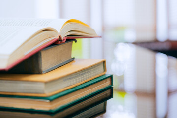 A stack of several books is placed on a table, with the top book left open