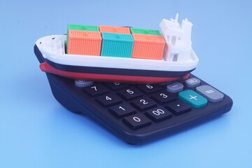 Cargo ship with containers on black calculator on blue background. Sea ​​transportation budget and price concept.	