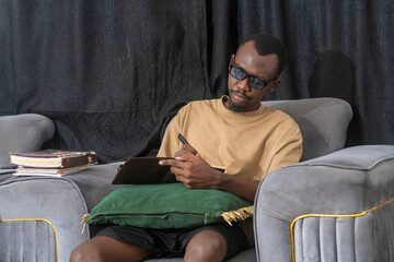 man writing in a notebook while sitting in living room.