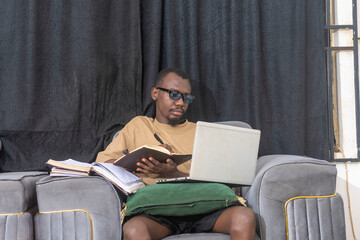 Male writing ideas in a notebook, surrounded by books and a laptop.