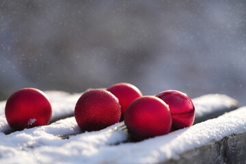 Red Christmas ornaments resting on a snowy wooden surface, glistening in soft winter light, creating a festive and cozy holiday atmosphere with seasonal charm