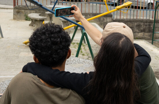 Man with his niece and his friend taking a selfie from behind in a park, capturing an everyday social moment outdoors with mobile technology