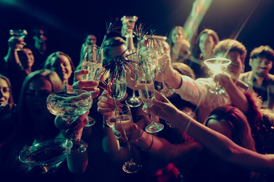 Crowd dancing with raised hands in colorful party lights. Concept of New Year party energy, freedom, nightlife culture, music events and holiday entertainment.