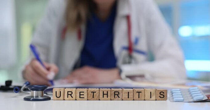 Woman doctor prepares list of treatment instructions for patient with urethritis. Word Urethritis formed from wooden blocks near stethoscope on table