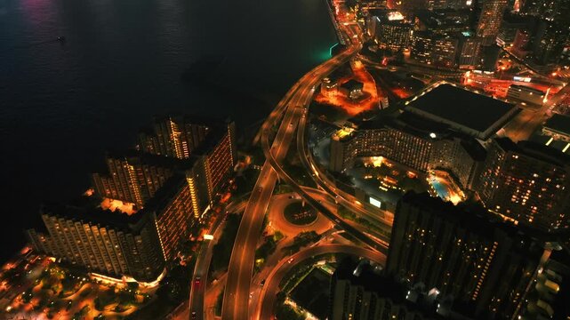Aerial view of the vibrant cityscape and the harbor, showcasing the illuminated buildings and roads contrasting against the dark water, Kowloon, Kowloon, Hong Kong.
