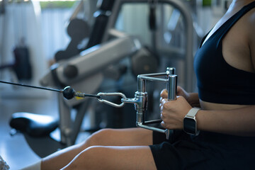 Closeup woman exercising back muscles on seated Row Machine in gym