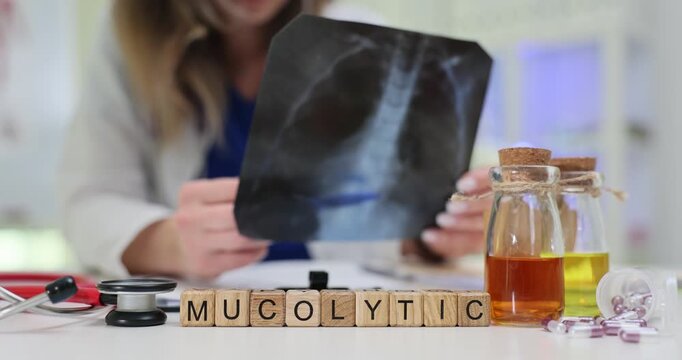 Doctor studies radiographic image comparing lung fields. Wooden blocks forming word Mucolytic rest on table as indication of recommended therapy