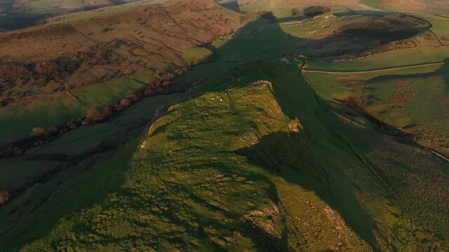 Aerial view of Mam Tor ridge at sunset, casting long shadows across the dramatic landscape, contrasting textures and tones, Buxton, England, United Kingdom.