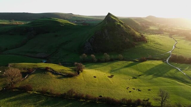 Aerial view of Chrome Hill and fields, a tapestry of verdant green hills and winding paths illuminated by the soft glow of the setting sun, Buxton, England, United Kingdom.
