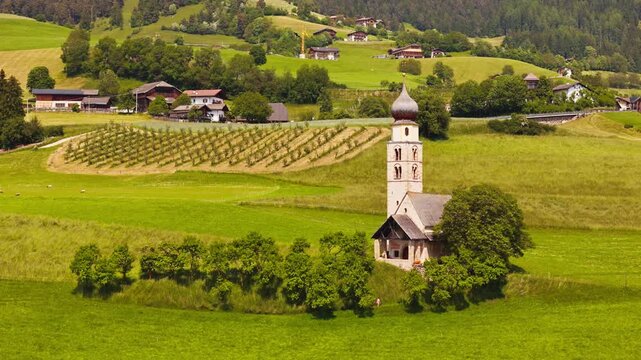 Aerial drone view of St. Valentin church surrounded farm fields in Dolomites Alpe di Suisi. South Tyrol, Italy