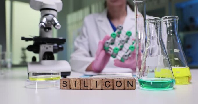 Wooden cubes form term Silicon identifying focus of analysis. Woman laboratory worker carefully examines artificial molecular model near microscope