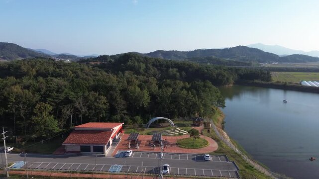 Aerial drone view of a calm lake and lakeside park surrounded by forested hills in rural South Korea