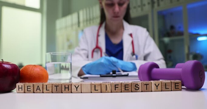Doctor prescribes balanced diet and regular workouts. Wooden blocks forming phrase Healthy Lifestyle rest on table near fresh fruit and dumbbell