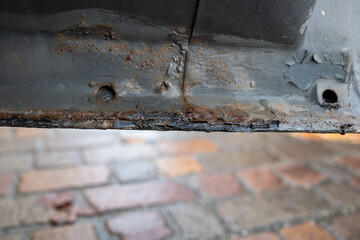 Rust and corrosion damage on the bottom edge of a car's left side door. Close up, low, wide angle view, no people