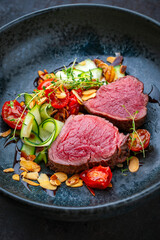 Fine dry aged beef filet steak rare tataki style cut tagliata with sliced zucchini, tomato and almonds served as close-up on a design plate
