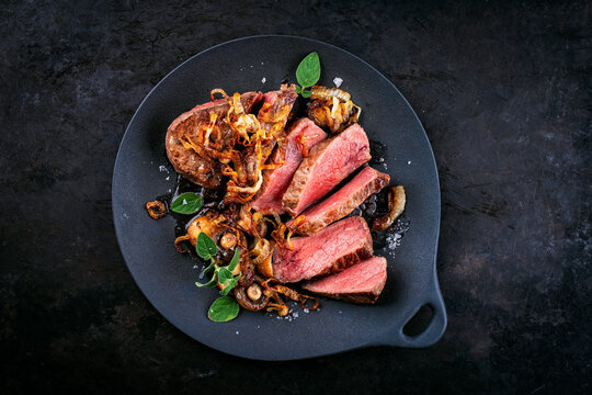 Zwiebelrostbraten roast beef - sirloin beef steak braised with fried onion rings and mushrooms served as top view in a design plate