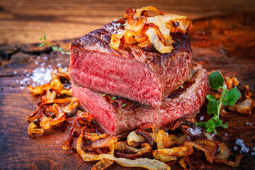 Zwiebelrostbraten roast beef - sirloin beef steak braised with fried onion rings served as close-up on an old wooden cutting board