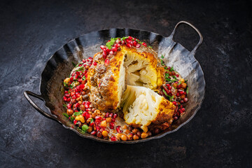Vegetarian dish - whole oven baked roasted cauliflower with tahini sauce, chickpeas and pomegranate served as close-up in a rustic iron skillet pan
