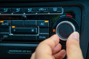 lose-up hand adjusting temperature dial car’s climate control system, set 19C, with illuminated buttons for AC, AUTO, dual-zone settings, Climate comfort, User interface design, Automotive ergonomics