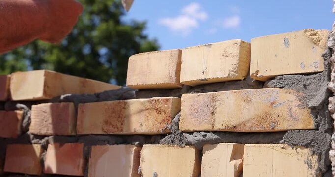 Professional construction worker is laying bricks while building a wall at a construction site. Close up of bricklayer using masonry tools to apply mortar and align the bricks with precision.