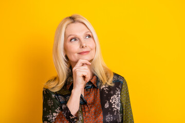 Elegant mature woman with blonde hair thoughtful pose wearing patchwork dress yellow background looking to the side with a gentle smile and style