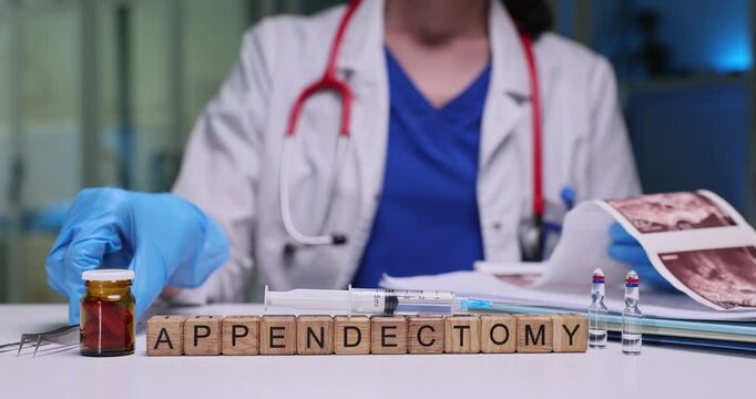 Doctor places surgical tweezers on table and studies patient ultrasound images. Miniature wooden cubes arranged on table form word Appendectomy