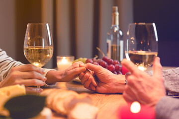 Close up cropped shot of the table during romantic dinner with lover`s hands with glasses of wine and food. Love and relationship, dating concept. Anniversary, proposal, Valentine`s Day celebration