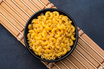 Raw macaroni pasta on black stone background