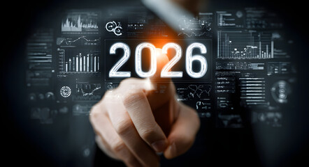 A businessmans finger touching a glowing 2026 on a futuristic digital interface, surrounded by business analytics icons, representing future planning and goal setting