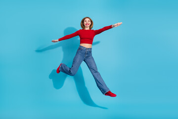 Fototapeta premium Cheerful young woman in stylish red outfit poses joyfully on a vibrant blue background showcasing casual fashion