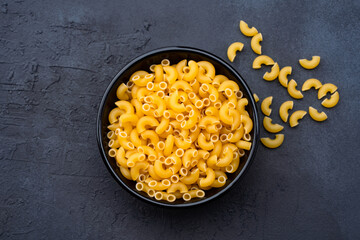 Raw macaroni pasta on black stone background