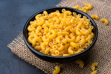 Raw macaroni pasta on black stone background