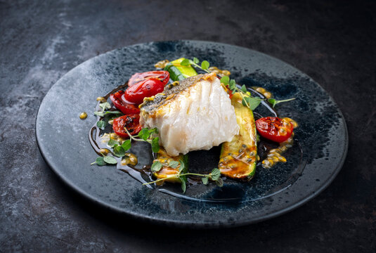 Fried skrei cod white sea fish filet with green vegetable and tomato, rice passion fruit relish umami sauce  Mediterranean dish recipe