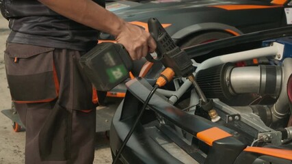 Technician's hands using an air tool to blow dust and debris off a car engine during maintenance or detailing.
