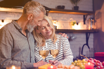 Passionate mature caucasian couple during romantic date in the kitchen. Loving husband spouse kissing cuddling embracing hugging his wife girlfriend while dining on special event, anniversary
