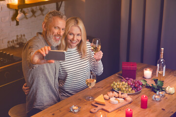 Lovely mature couple taking selfie having romantic date in the kitchen. Vlogging blogging on St Valentine`s Day, anniversary celebration. Online social media posting, videocall