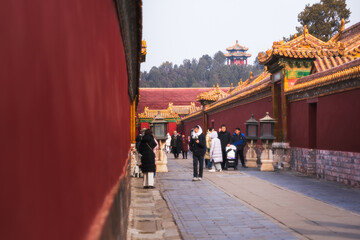 View of ancient red walls enclosing pathways where people stroll, crowned by ornate golden roofs and distant pavilions, Beijing, Beijing, China.