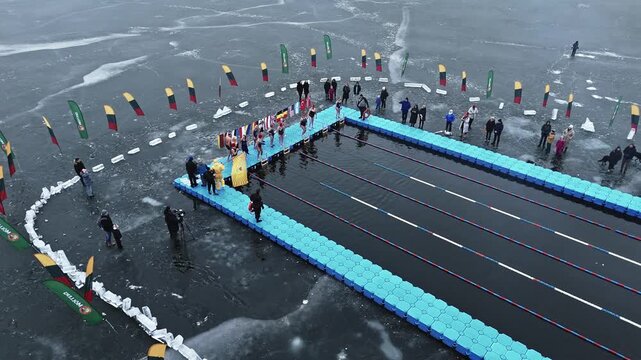 Trakai, Lithuania - 01 March 2025: Aerial view of swimmers diving into the icy waters of Lake Galve during a winter swimming competition.