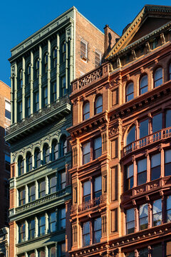 Cast-iron and brick facades along Broadway in the NoHo Historic District of Manhattan, featuring detailed historic architecture in warm sunlight. New York City, USA