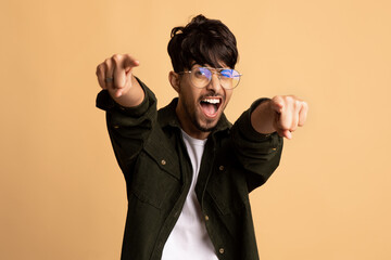 A young man stands against a plain background, expressing joy with a wide smile and playful...