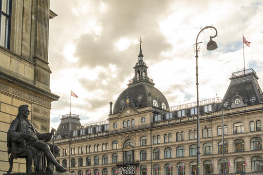 Copenhagen, Denmark - 30 September 2025: View of Magasin du Nord department store, its facade adorned with flags, juxtaposed against the somber statue in the foreground, under a cloudy sky.