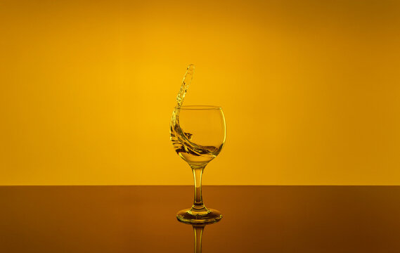Dynamic splash of clear water in a wine glass on a vivid golden yellow background. Creative high-speed studio photography of liquid motion, transparency, and energy inside a goble