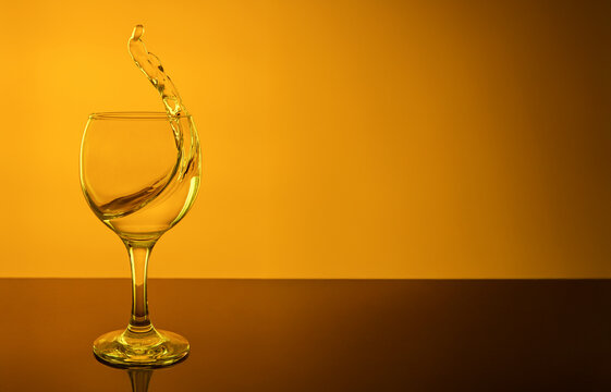 Dynamic splash of clear water in a wine glass on a vivid golden yellow background. Creative high-speed studio photography of liquid motion, transparency, and energy inside a goble