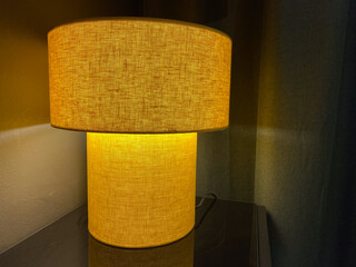 Illuminated beige table lamp on dark surface with subtle texture and warm glow