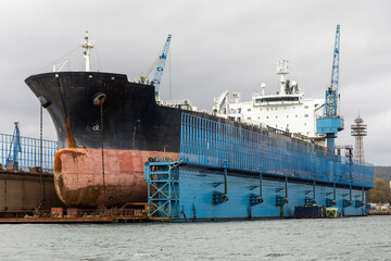 A massive tanker vessel with a bulbous bowin in dry dock for maintenance at a commercial shipyard. Shipbuilding, Repair and Maritime industry concept.