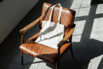 Canvas tote bag mockup on leather chair with dramatic natural light shadows