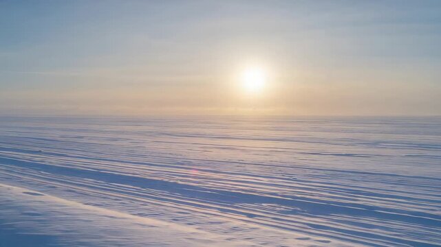 Panning camera moving slowly over frozen plain, showing low sun and parallel snow ridges at sunrise