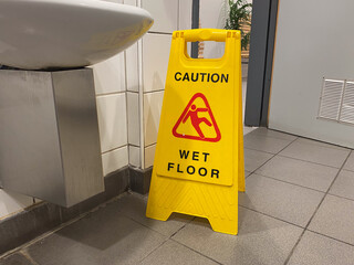 Yellow caution wet floor sign in restroom with tiled flooring