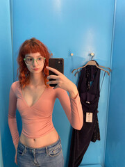 Young caucasian female taking selfie in dressing room with blue walls and dresses