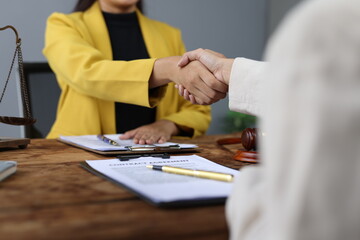 Two lawyers shaking hands after signing a contract agreement in their office, with legal documents,...